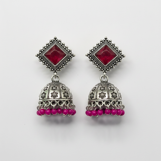 Oxidized silver ruby red stone jhumka earrings with magenta bead drops on white background